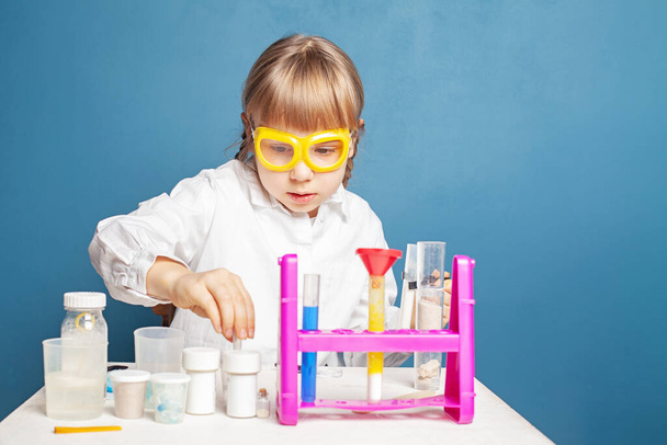 Серйозна школярка проводить наукові експерименти на синьому фоні. Наука та концепція освіти - Фото, зображення