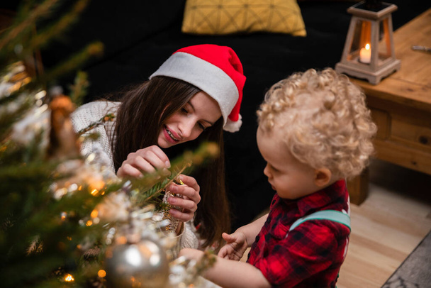Sestra pomáhá jejímu mladému bratrovi pověsit ozdoby pro vánoční stromeček. - Fotografie, Obrázek