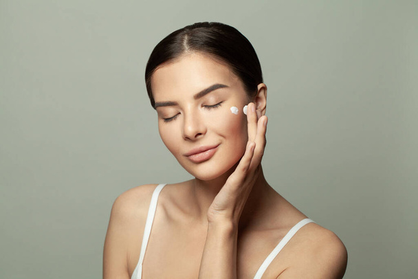 Zdrowa kobieta nakłada krem nawilżający na twarz. Koncepcja leczenia twarzy i opieki zdrowotnej - Zdjęcie, obraz