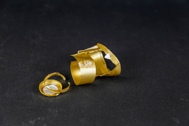 A tattered gold wine bottle capsule against a black background. - Photo, Image