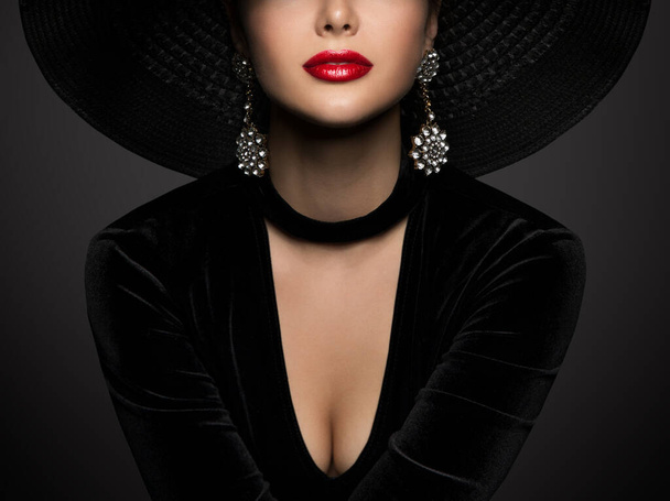 Fashion Woman Face Portrait with Red Lips Close up. Beauty Model in Black Dress and Wide Brim Hat. Elegant Lady in Silver Crystal Jewelry Earrings and Necklace over Dark Gray Background - Foto, Bild