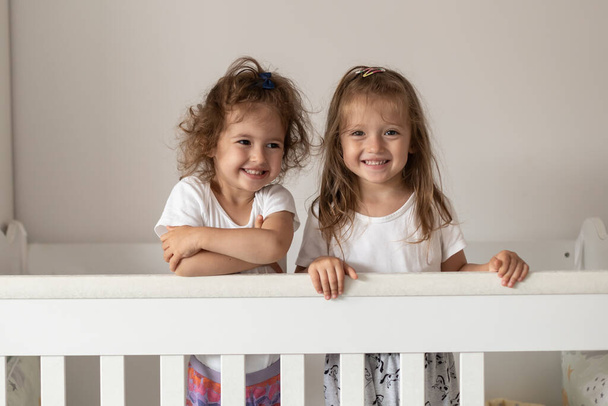 Happy fraternal twins sisters having fun, standing in crib. Happy gitls - 写真・画像