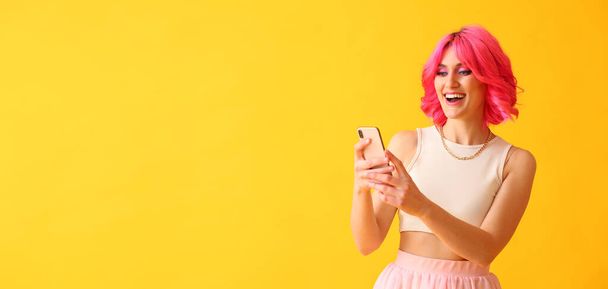 Stylish woman with bright pink hair and mobile phone on yellow background with space for text - 写真・画像