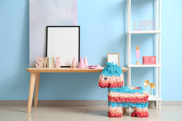 Stůl s rámečkem, regálovou jednotkou a mexickou pinatou na narozeninovou oslavu u modré zdi - Fotografie, Obrázek