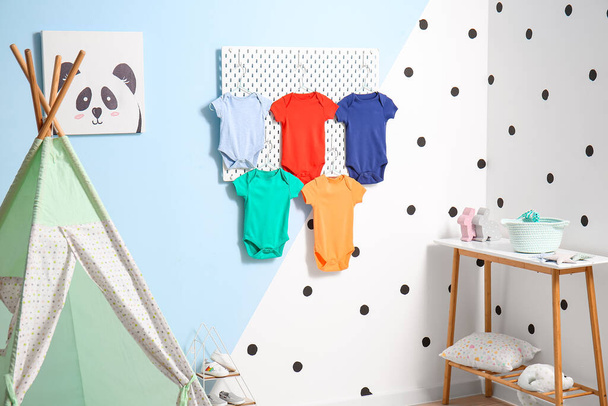 Pegboard με βρεφικές φόρμες κρεμασμένες στον χρωματικό τοίχο του παιδικού δωματίου - Φωτογραφία, εικόνα