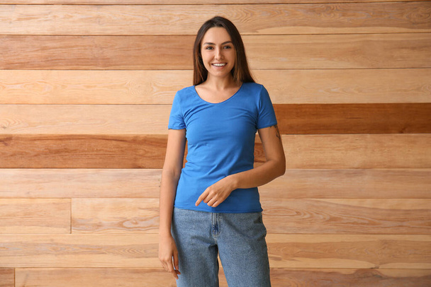 Jonge vrouw in blanco t-shirt op houten achtergrond - Foto, afbeelding