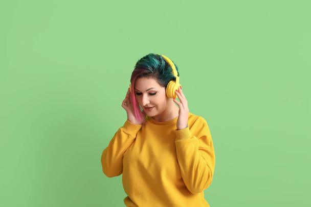 Piękna kobieta z nietypowymi włosami słuchająca muzyki na zielonym tle - Zdjęcie, obraz