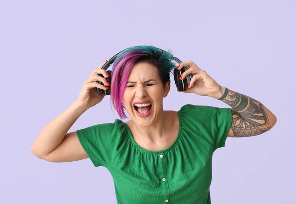 Belle femme aux cheveux inhabituels et tatouage écoutant de la musique sur fond de couleur - Photo, image