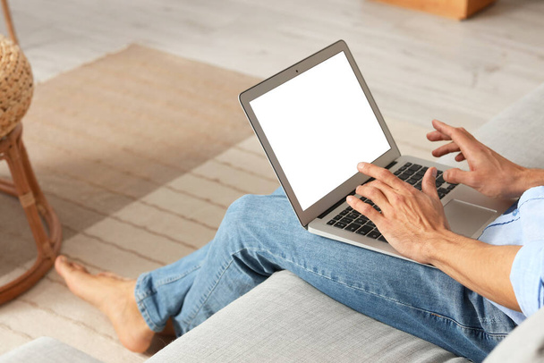 Молодой босоногий мужчина с ноутбуком на диване дома - Фото, изображение