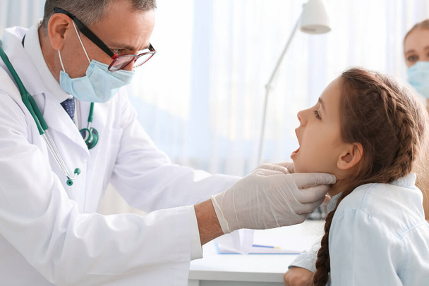 Dokter onderzoeken klein meisje met zere keel in kliniek - Foto, afbeelding
