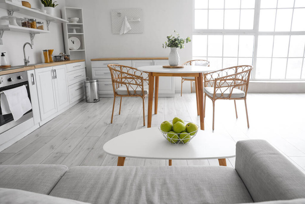 Kényelmes kanapé és asztal kosár friss almával a világos konyha belsejében - Fotó, kép