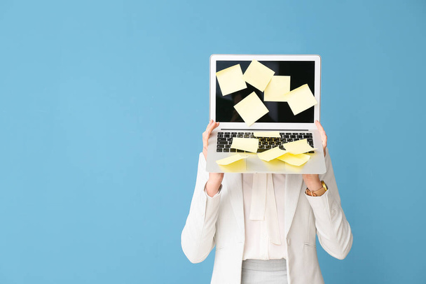 Young woman with sticky note papers on laptop against blue background - Foto, afbeelding