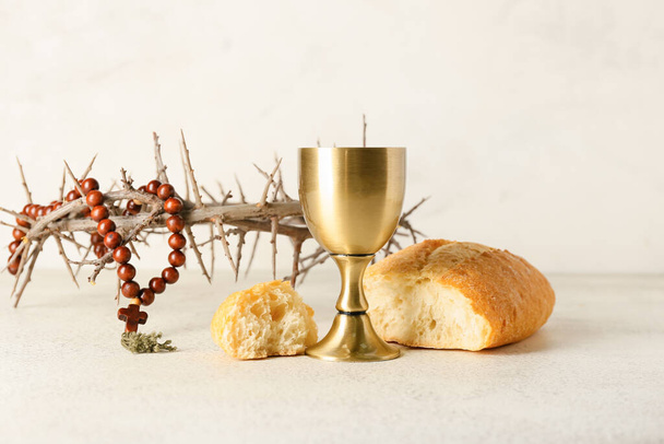 Cup of wine with bread, crown of thorns and rosary on light background - Photo, Image