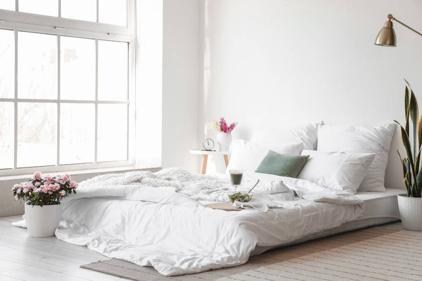 Интерьер светлой комнаты с красивыми цветами и завтраком на кровати - Фото, изображение