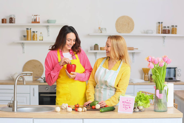 Feliz joven mujer y su madre cocinando juntos en la cocina en casa. Celebración del Día Internacional de la Mujer - Foto, imagen