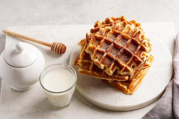 Сухой завтрак - свежие домашние пельмени с медом и сахарной пудрой, сложенные на белой круглой мраморной доске, и маленький стакан с молоком - Фото, изображение