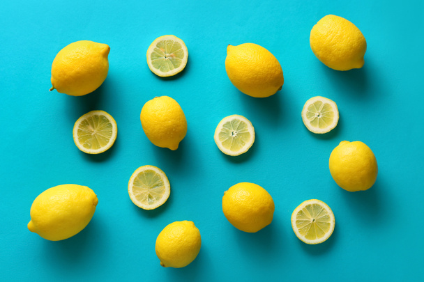 Ripe lemons and slices on blue background, top view - 写真・画像
