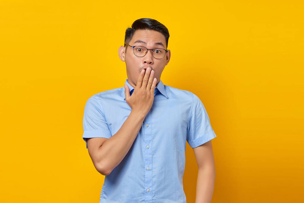 портрет шокованого молодого азіатського чоловіка в окулярах, що закривають рот обома руками ізольовано на жовтому тлі. бізнесмен і концепція підприємця
 - Фото, зображення
