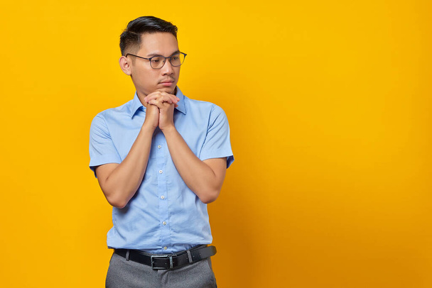 眼鏡をかけたアジア系の青年の肖像画は黄色の背景に孤立した顎の下に手を置いている。ビジネスマンや起業家の考え方 - 写真・画像