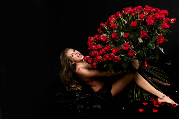 Sensual woman with red lips with red rose, black background. Beautiful sexy woman holding large bouquet of red roses on black background. Valentines day. Holiday birthday day. - Foto, Imagem