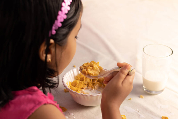 Focus selettivo su un cucchiaio di cornflakes tenuto in mano da una bambina indiana - Foto, immagini