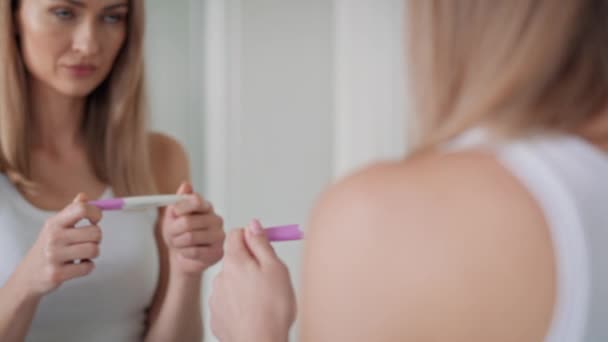 Молодая женщина стоит перед зеркалом в ванной и ждет результатов теста на беременность. Съемка с красной гелиевой камерой в 8K.     - Кадры, видео