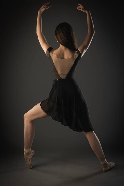 Elegant ballerina with pointe shoes is doing a asymmetrical pose from the back - Foto, Imagen