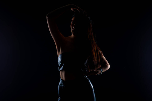Silhouette di giovane e attraente ragazza in posa in studio su sfondo nero - Foto, immagini