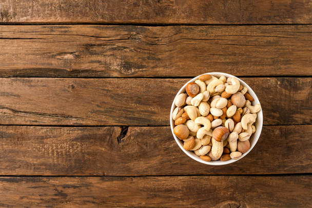 Various kinds of nuts (almonds, pistachios, peanuts, hazelnuts and cashews) in bowl on wooden table. Close up - Photo, image