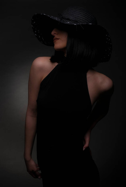 Beautiful and elegant girl is posing in black dress and hat, in studio - Foto, Imagen