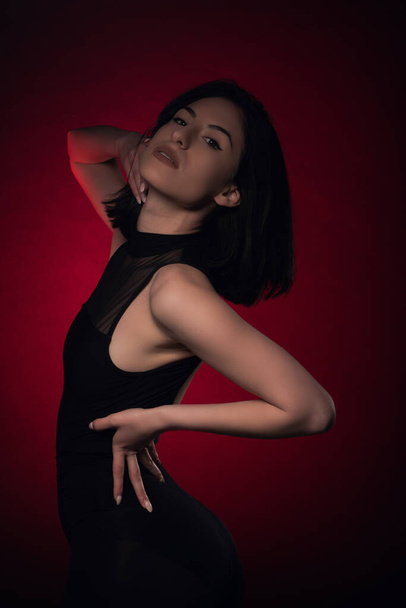Attractive and seductive girl is being sexy on set while posing on red background - 写真・画像