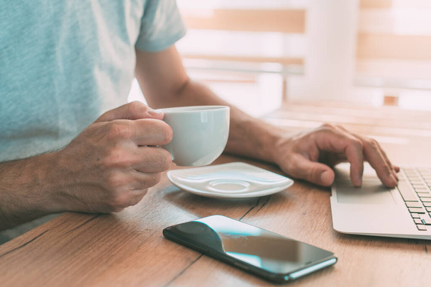 Freelancer juo kahvia ja työskentelee kotoa kannettavan tietokoneen aamulla, valikoiva keskittyminen - Valokuva, kuva
