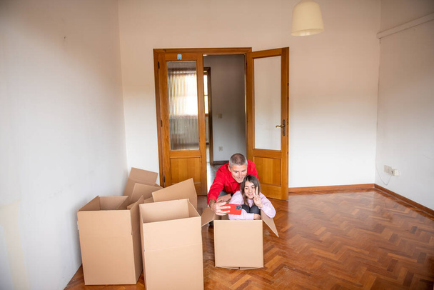 Moving to a new home concept. Young girl in a cardboard box smiling happy and playing with her father - Photo, Image