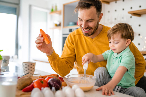 Young happy single father with a toddler boy having fun and preparing healthy food in kitchen at home. - Foto, immagini