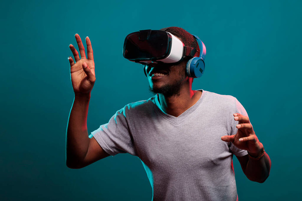 Genç adam VR gözlükleriyle fütüristik oyun oynamak için el kaldırıyor. - Fotoğraf, Görsel