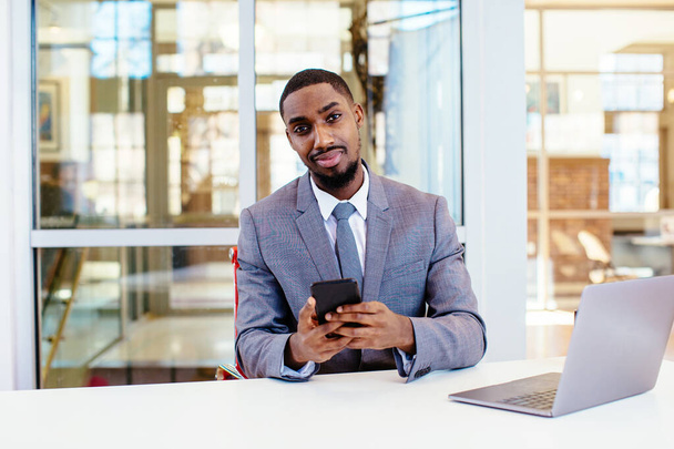 Genç bir Afro-Amerikan iş adamının portresi masada oturuyor ve akıllı telefon kullanıyor. - Fotoğraf, Görsel
