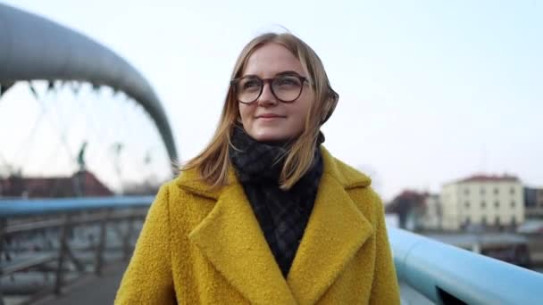 Beautiful young stylish blonde woman wearing beige coat and glasses standing near white street wall. Street fashion. - Footage, Video