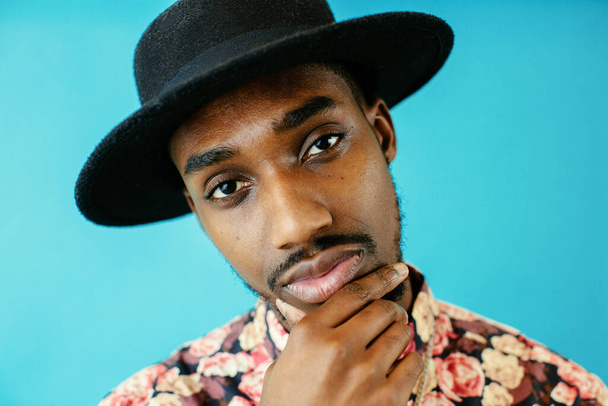 portrait of a young african american man wearing black hat against blue background - 写真・画像