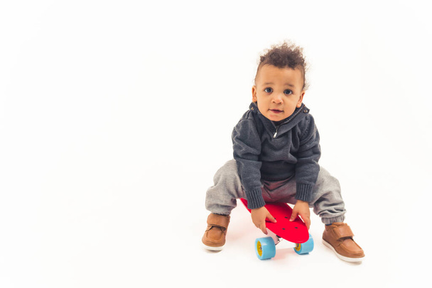 cute curly toddler sitting on the skateboard and looking into the camera studio shot full shot white background copy space - Photo, image
