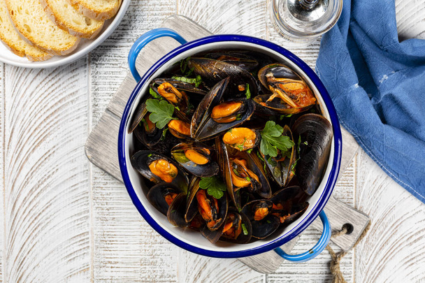 Cooked seafood mussels in a blue pan, with parsley and tomato sauce. Clams in the shells.  Bread. Top view. - Zdjęcie, obraz