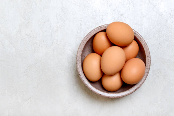 Bruine rauwe eieren in een kom op een lichte ondergrond. Bovenaanzicht met kopieerruimte. - Foto, afbeelding