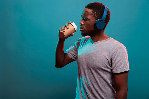 Ξέγνοιαστος τύπος που ακούει μουσική στα ακουστικά και πίνει καφέ. - Φωτογραφία, εικόνα