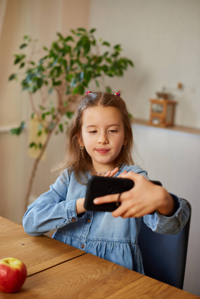 Happy smiling little girl holding smartphone having video call with friend distantly, online talk with grandmother about healthy food, communication, using smartphone, technology concept - Фото, изображение