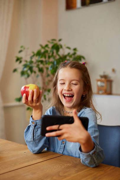 Όμορφη νεαρή κοπέλα μαγνητοσκόπηση blog της εκπομπή σχετικά με υγιεινό φαγητό στο σπίτι. Μικρό κορίτσι που επιλέγουν μεταξύ γλυκό κέικ και φρέσκο κόκκινο μήλο, Υγιεινή διατροφή συνήθεια, έννοια της σωστής διατροφής - Φωτογραφία, εικόνα