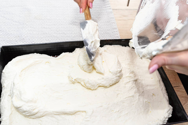 Een vrouw giet de gemengde wrongel en slagroom in een gebakken chocoladetaart in een bakplaat. - Foto, afbeelding
