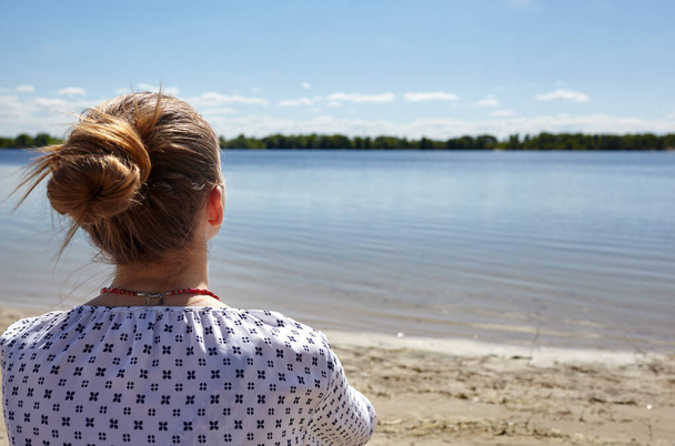 Girl sitting on the coast and looking into the distance. Young woman resting at water. Enjoy life, having fun, leisure, relaxation, lifestyle concept. Rear view - Foto, imagen