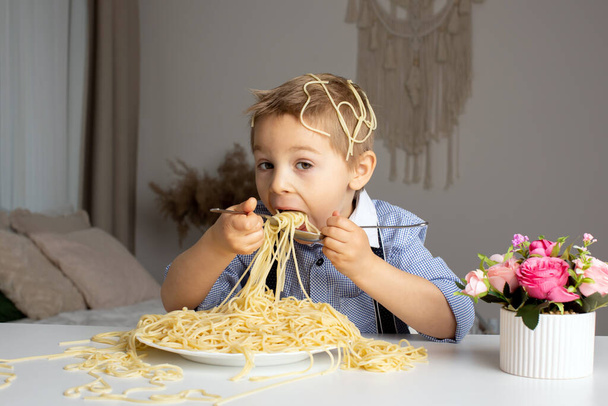 Cute preschool child, blond boy, eating spaghetti at home, making a mess everywhere, funny moments - Фото, изображение