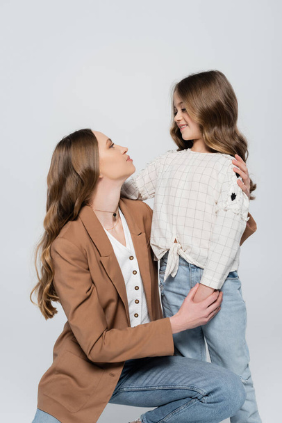 mother and daughter with long hair embracing and looking at each other isolated on grey - Photo, Image