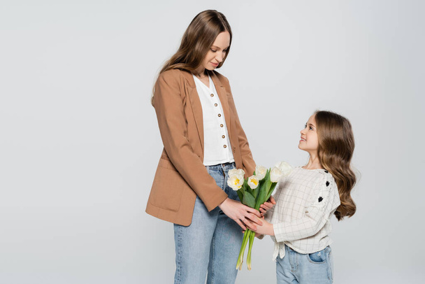 smiling girl presenting tulips to mother isolated on grey - Fotografie, Obrázek