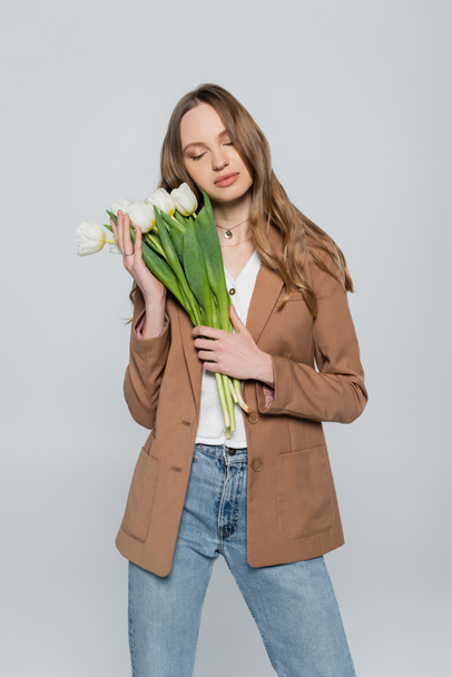 stylish woman with closed eyes posing with tulips isolated on grey - Фото, зображення
